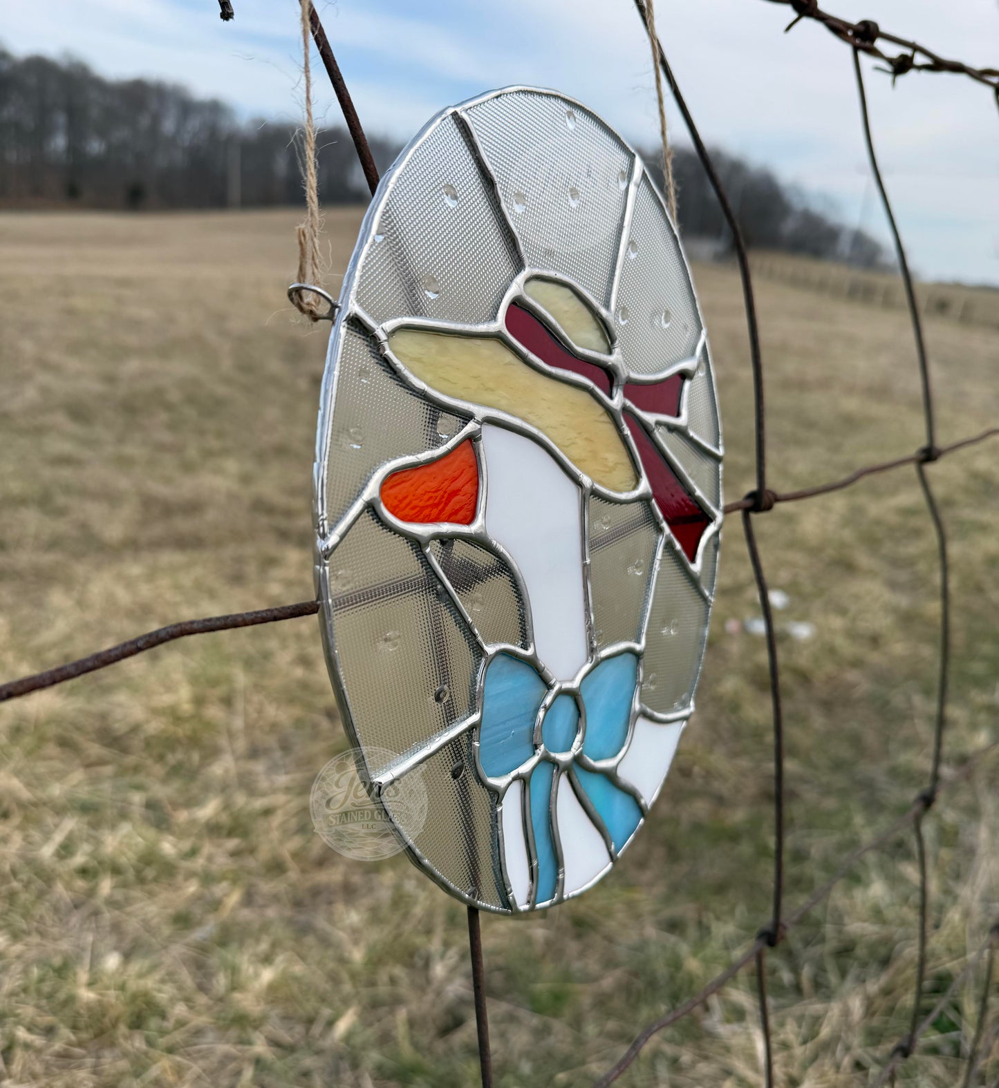 Stained glass duck decoration on a wire fence with a field in the background
